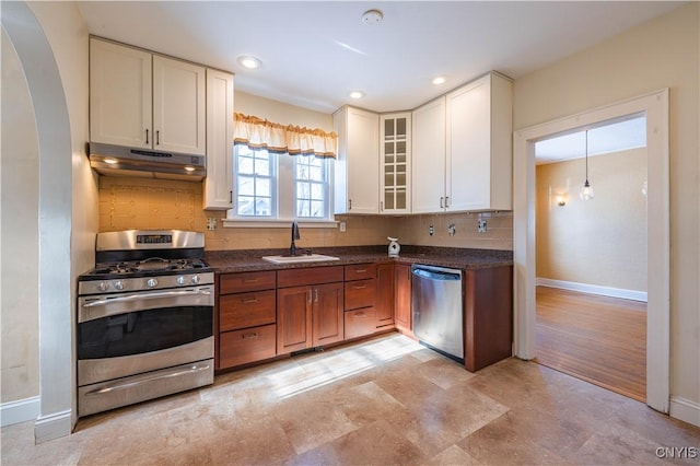 kitchen featuring appliances with stainless steel finishes, a sink, baseboards, under cabinet range hood, and backsplash