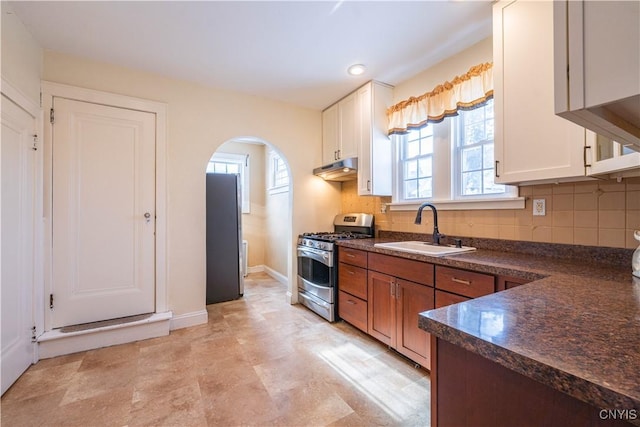kitchen featuring appliances with stainless steel finishes, a sink, dark countertops, arched walkways, and tasteful backsplash