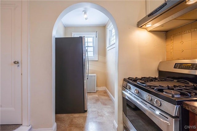 kitchen with appliances with stainless steel finishes, under cabinet range hood, arched walkways, and baseboards