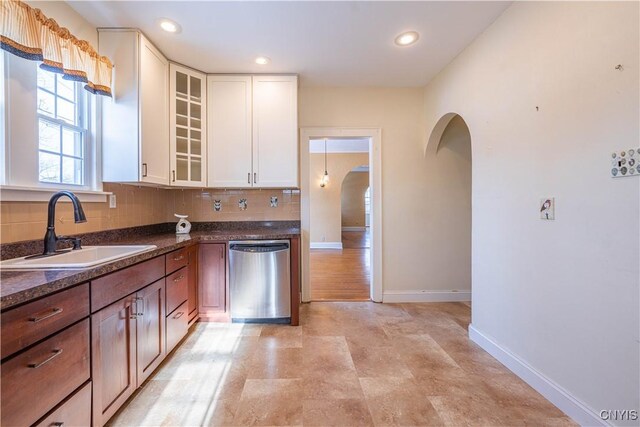kitchen with stainless steel dishwasher, a sink, arched walkways, baseboards, and backsplash