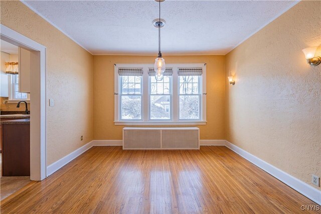 unfurnished dining area featuring a textured wall, radiator heating unit, wood finished floors, baseboards, and a textured ceiling