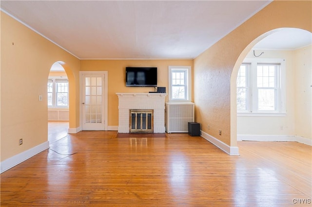 unfurnished living room with wood finished floors, crown molding, a fireplace, arched walkways, and baseboards