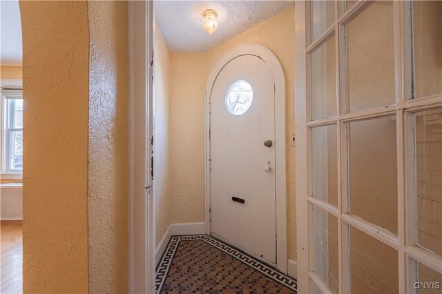doorway to outside with a textured wall, baseboards, and arched walkways