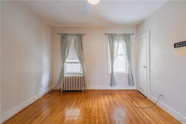 empty room with radiator heating unit, light wood-style floors, and baseboards