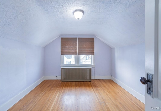 bonus room featuring radiator heating unit, a textured ceiling, wood finished floors, baseboards, and vaulted ceiling