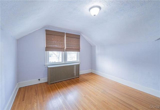 bonus room featuring a textured ceiling, radiator heating unit, wood finished floors, lofted ceiling, and baseboards