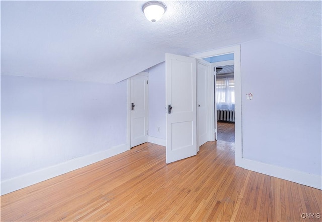 bonus room featuring radiator heating unit, baseboards, light wood-style floors, a textured ceiling, and vaulted ceiling