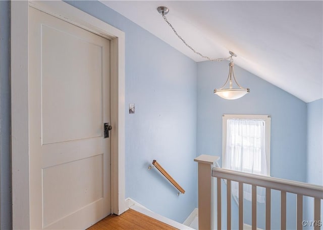 corridor featuring an upstairs landing, vaulted ceiling, and light wood-style flooring