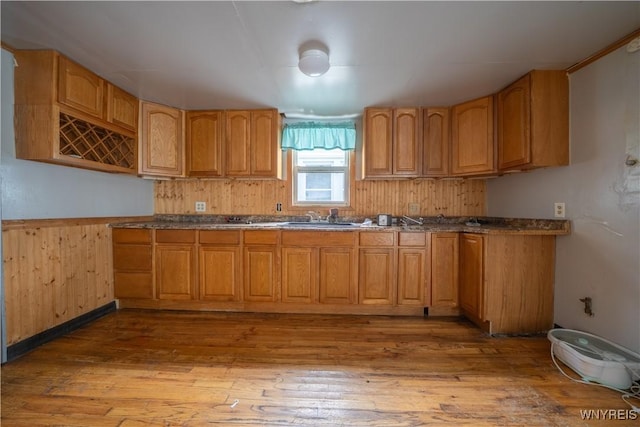 kitchen with wood finished floors, a sink, wood walls, and brown cabinets