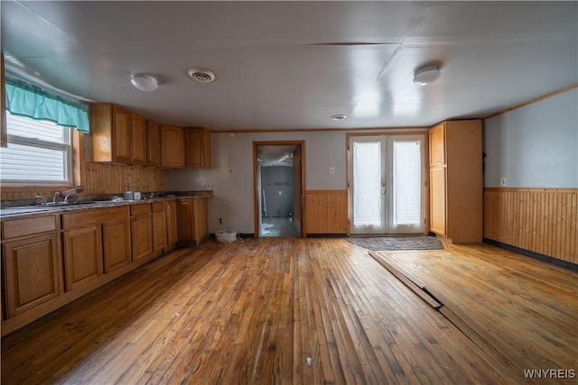 kitchen featuring a sink, light wood-style flooring, wainscoting, brown cabinetry, and wood walls