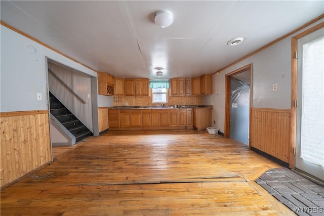 kitchen with light wood finished floors, wainscoting, wood walls, and ornamental molding