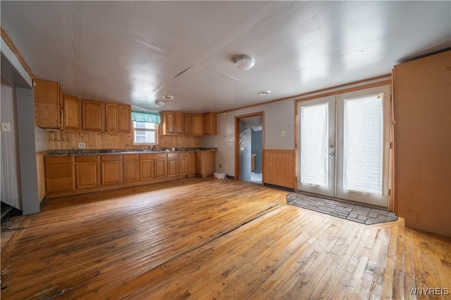 kitchen with light wood-type flooring, french doors, brown cabinetry, wainscoting, and dark countertops