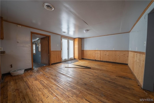 empty room featuring wainscoting, wood-type flooring, wood walls, and crown molding