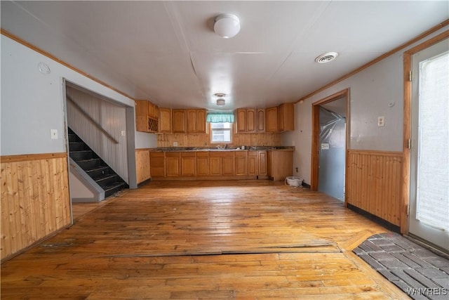 kitchen featuring light wood finished floors, a wainscoted wall, wood walls, and ornamental molding