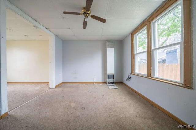 carpeted spare room with baseboards, a drop ceiling, and a ceiling fan