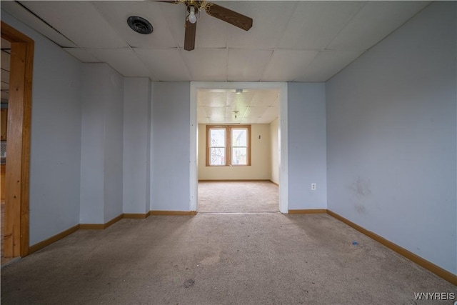 carpeted empty room with a paneled ceiling, a ceiling fan, and baseboards