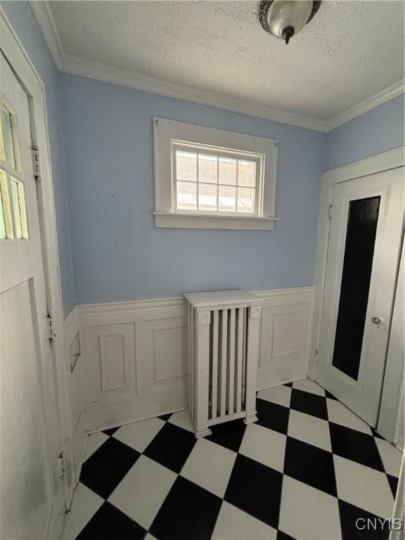 hallway featuring tile patterned floors, a wainscoted wall, a textured ceiling, and ornamental molding