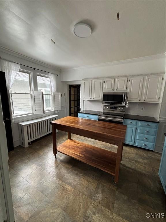 kitchen with stainless steel appliances, radiator, dark countertops, stone finish flooring, and ornamental molding