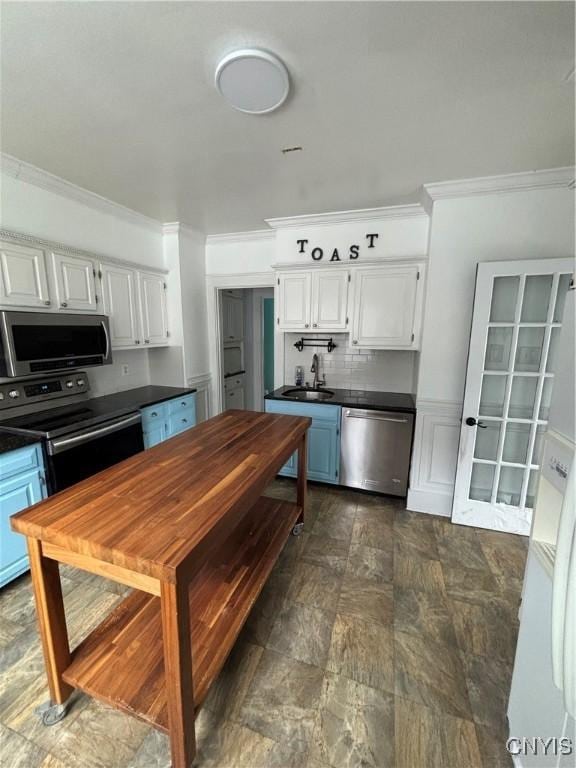 kitchen featuring stainless steel appliances, a sink, dark countertops, ornamental molding, and stone finish flooring