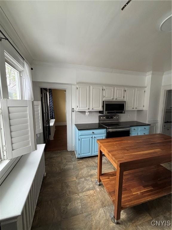 kitchen with appliances with stainless steel finishes, dark countertops, white cabinetry, ornamental molding, and baseboards
