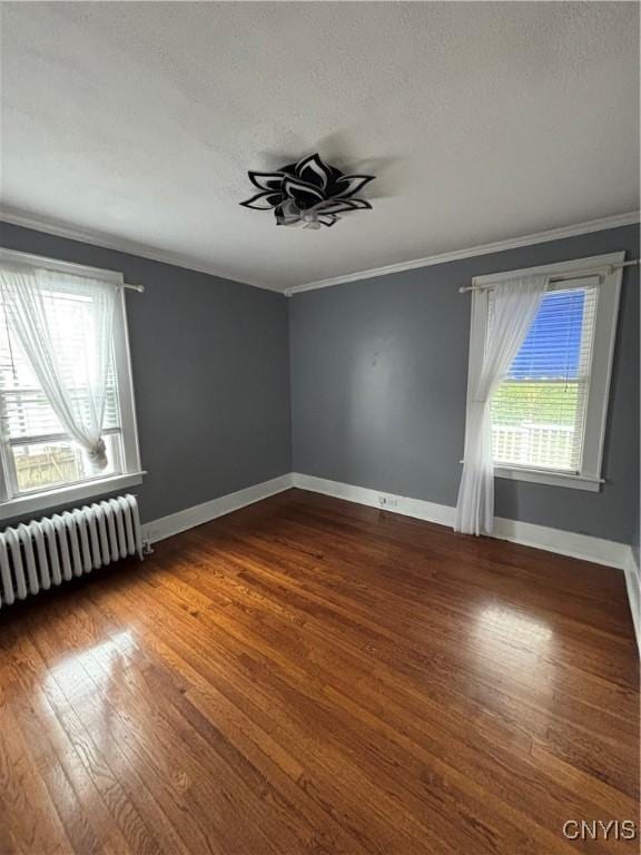 empty room with radiator, ornamental molding, healthy amount of natural light, wood finished floors, and a textured ceiling