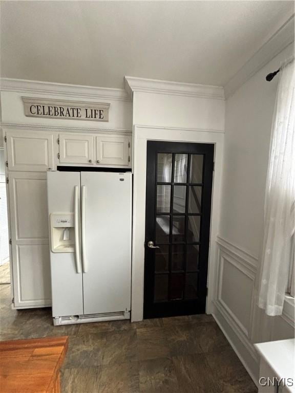 kitchen featuring white refrigerator with ice dispenser, ornamental molding, wainscoting, and white cabinetry