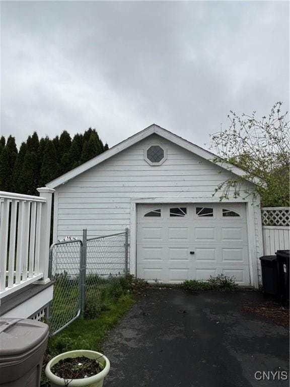 detached garage featuring asphalt driveway and fence