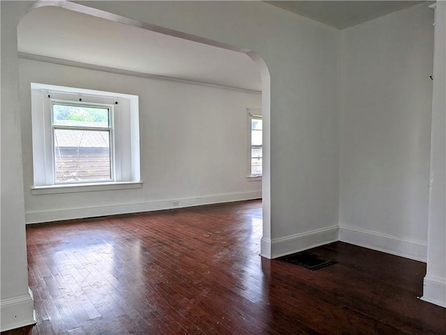 spare room with healthy amount of natural light, arched walkways, hardwood / wood-style floors, and crown molding