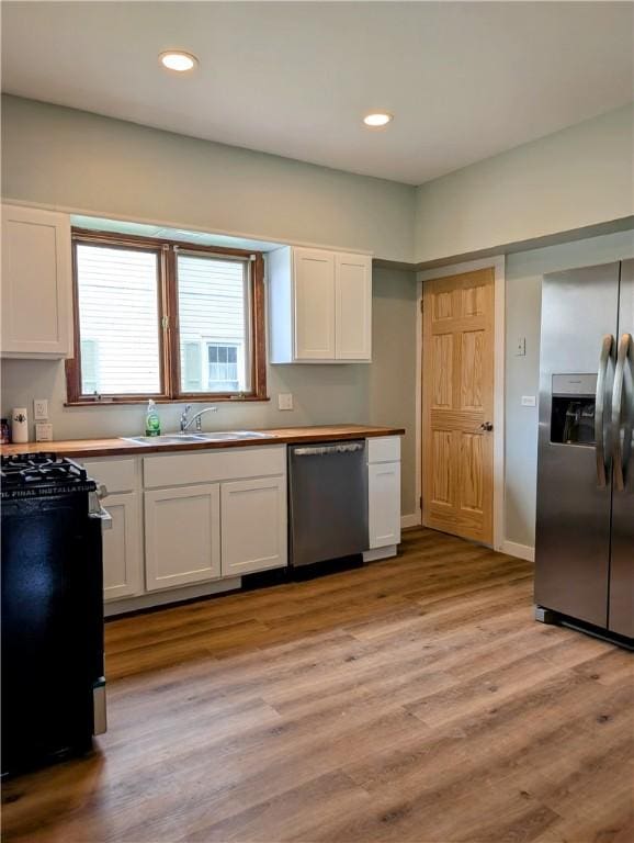 kitchen featuring appliances with stainless steel finishes, white cabinetry, a sink, light wood finished floors, and recessed lighting