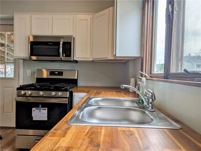 kitchen featuring wood counters, appliances with stainless steel finishes, white cabinets, and a sink