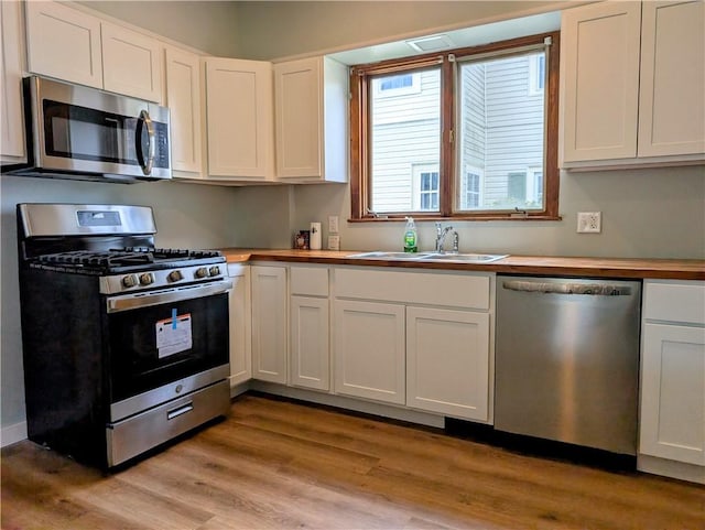 kitchen featuring stainless steel appliances, a sink, wooden counters, light wood-type flooring, and white cabinets
