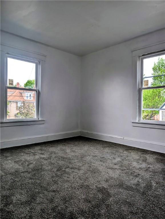 unfurnished room with dark colored carpet, plenty of natural light, and baseboards