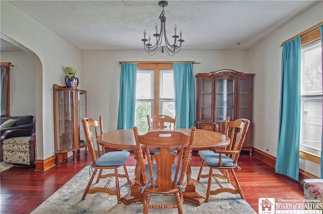 dining room with wood-type flooring, arched walkways, a chandelier, baseboards, and a textured ceiling