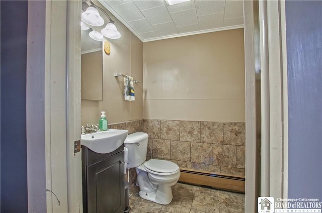 bathroom featuring baseboard heating, crown molding, toilet, vanity, and wainscoting