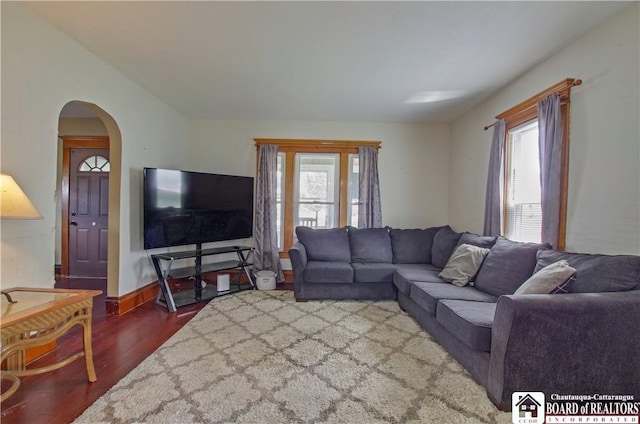 living room with wood finished floors, plenty of natural light, arched walkways, and baseboards