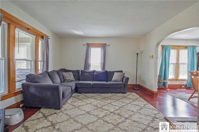living room featuring arched walkways, plenty of natural light, wood finished floors, and baseboards