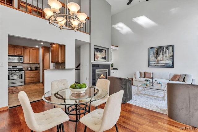 20 Harbour Pointe, Buffalo, NY 14202 - dining room with a chandelier, a towering ceiling, a warm lit fireplace, light wood-style flooring, and a ceiling fan