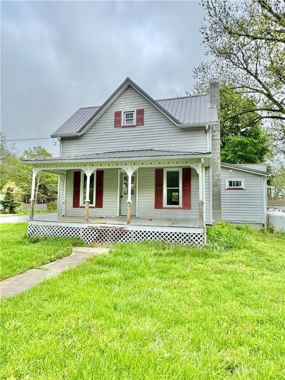 view of front of home featuring a chimney, covered porch, metal roof, and a front lawn