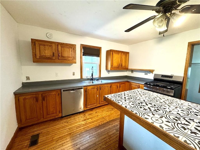 kitchen with appliances with stainless steel finishes, a sink, light wood-type flooring, and brown cabinetry