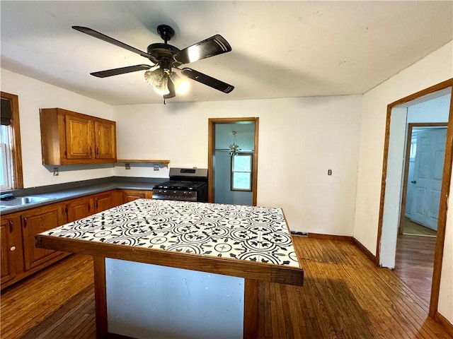 kitchen featuring stainless steel gas range oven, dark wood-style floors, brown cabinetry, a sink, and baseboards