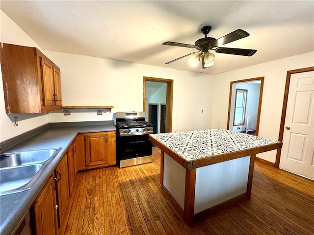 kitchen featuring stainless steel gas range, a sink, brown cabinetry, dark wood finished floors, and a kitchen island