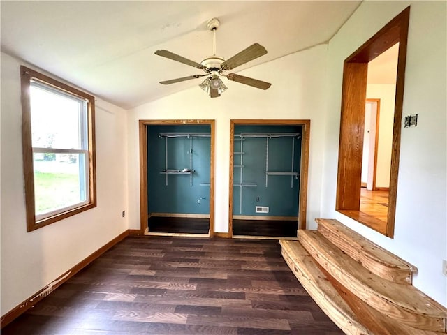 unfurnished bedroom with lofted ceiling, dark wood-type flooring, baseboards, ceiling fan, and multiple closets