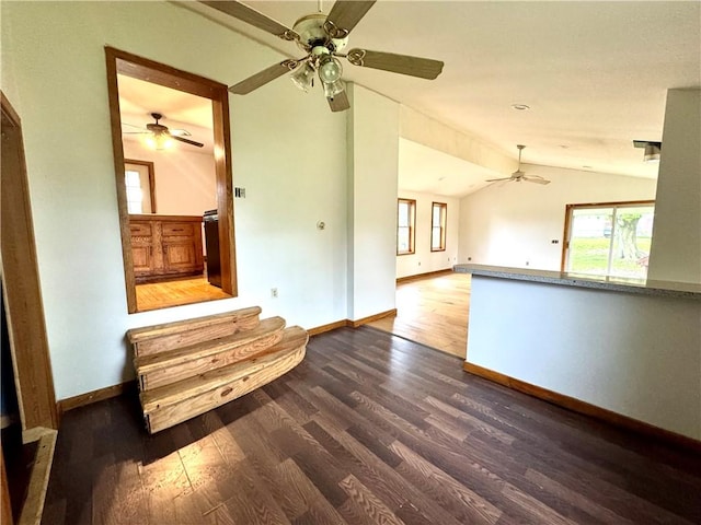 unfurnished living room with a ceiling fan, lofted ceiling, dark wood-style floors, baseboards, and plenty of natural light