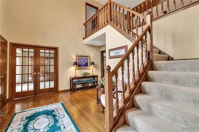 stairway with french doors, a high ceiling, wood finished floors, and baseboards