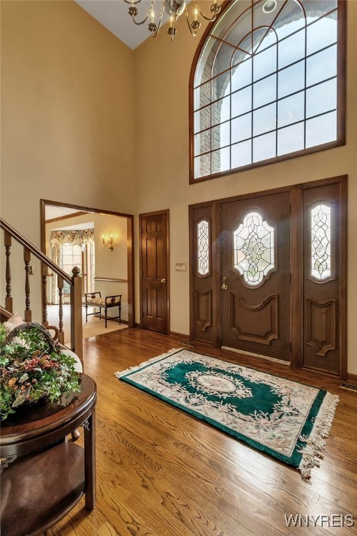 foyer entrance with a towering ceiling, a chandelier, wood finished floors, stairs, and baseboards