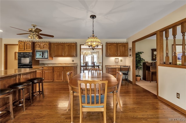 dining area with dark wood-style floors, a ceiling fan, a chandelier, and baseboards