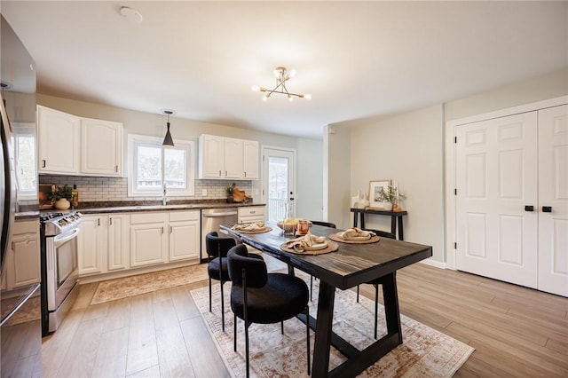 kitchen featuring appliances with stainless steel finishes, dark countertops, backsplash, light wood-style floors, and a chandelier