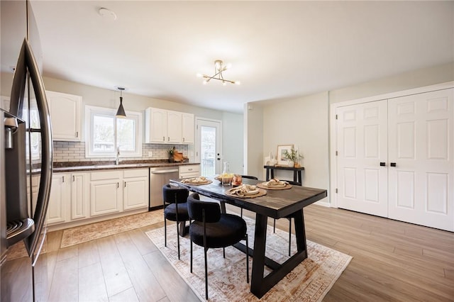 kitchen featuring freestanding refrigerator, stainless steel dishwasher, dark countertops, tasteful backsplash, and light wood-type flooring