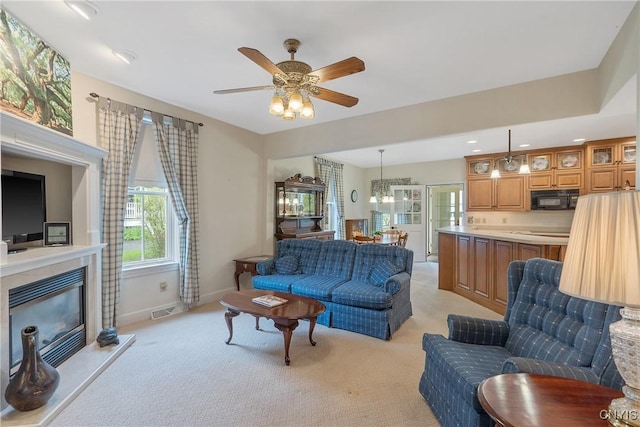 living room featuring light colored carpet, a glass covered fireplace, ceiling fan, baseboards, and a chandelier