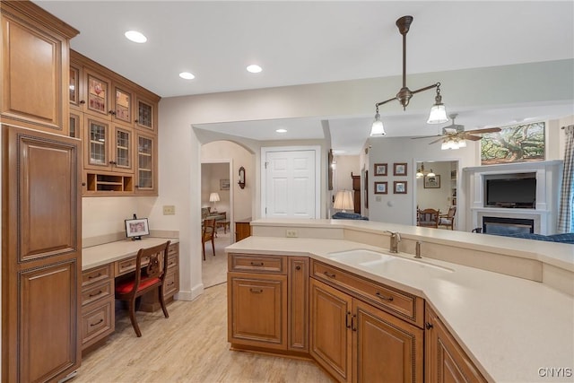 kitchen featuring brown cabinetry, arched walkways, a ceiling fan, light countertops, and a sink